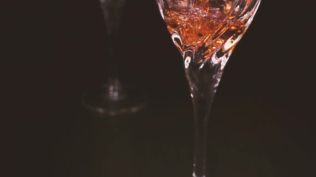 Slow motion Rose wine pours into the wine glass. The camera rises.