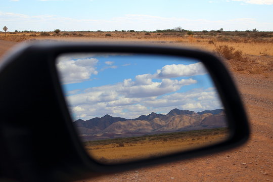 Landscape picture of a mountain range reflected in the side view mirror of a car, captured in Flinders Ranges, South Australia state, Australia