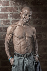 Tough muscular senior African American man with his shirt off dramatically lit against a brick wall