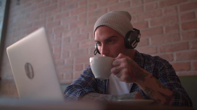 Cool hipster listening to podcast on his laptop, drinking coffee