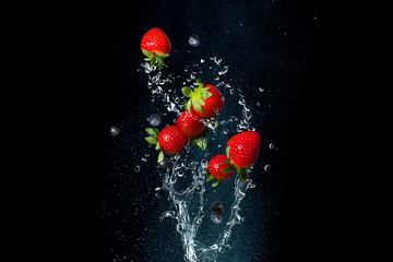 Fresh berries in splashes of water on black background. Juicy strawberries and blueberries