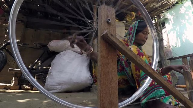 Pretty young woman turns spindle and spinning wheel, tracking shot side to top view. 2X slow motion. Bengal, India