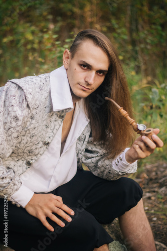 Sexy Long Haired Man With A Pipe In His Hands In The Woods In A