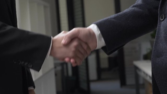 Two successful businessmen in suits are shaking hands in the office in the background, an African businessman, a Caucasian businessman. 60 fps