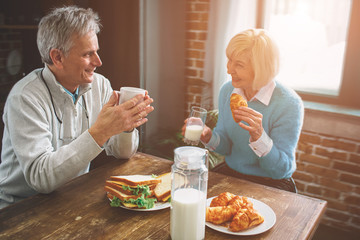 Another picture of nature old people sitting in the kitchen. THey are drinking milk and talking to each other. They are enjoying company of one another.