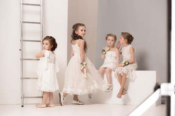 Little pretty girls with flowers dressed in wedding dresses