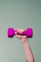 female lifting magenta colored dumbbell against teal background