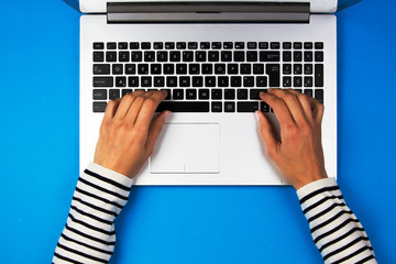 Woman hands typing on laptop computer on blue background