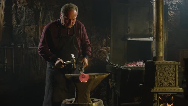 Blacksmith brings dripping hot metal from furnace and he beats a piece of hot metal with a hammer on an anvil. Shot on RED EPIC-W Helium Cinema Camera in Slow Motion.