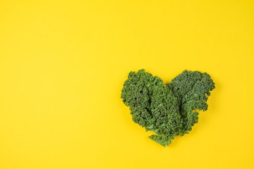 Fresh kale leaves in the shape of a heart on yellow background.
