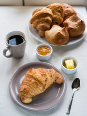 Continental breakfast with French croissants, butter, jam, black coffee and a basket of assorted French pastries on white table