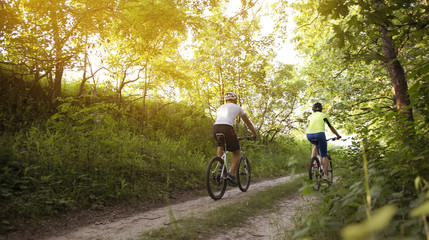 Fototapeta premium a woman and a man cycling in summer in the park on bicycles
