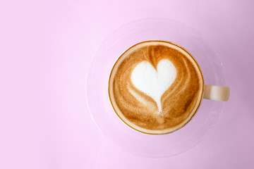 Top view of hot coffee latte with heart shaped latte art milk foam on pink pastel color sweet background.