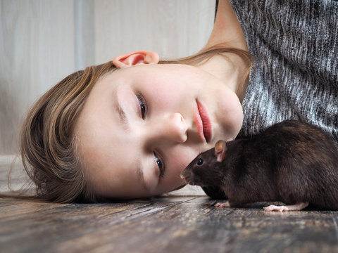 The girl lying on the floor looks at the rat