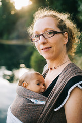 Obraz premium Blonde caucasian mom holding her colored child in a sling