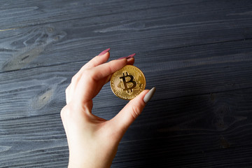 Bitcoin gold coin in female hand on the dark blue wooden background.
