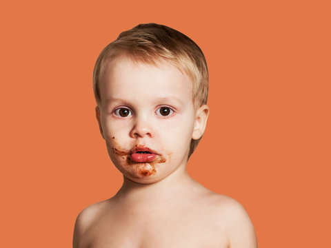 Cute Child Smeared Face In Chocolate. Isolated On Orange Background.