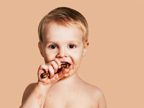 Cute Child Eating Chocolate With Smeared Face. Isolated On Beige Background.