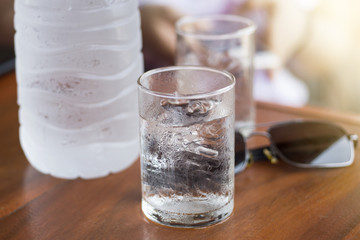 Glass of Iced cold water on the wooden table with water bottle and sun glasses in background, soft sunlight effect added. Refreshing cold water after being out in hot summer sun.