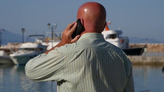 Businessman Talking to Mobile and Gesturing in a Harbor with Boats in Background