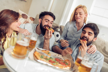 Happy friends eating pizza and watching tv at home