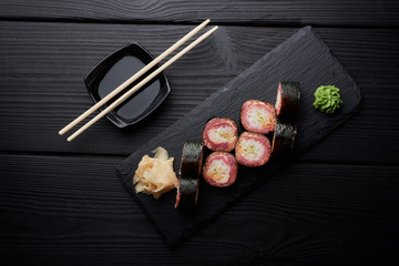 Fototapeta na wymiar Fresh sushi rolls served on black stone slate with chopsticks, top view. 