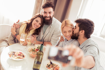 Smiling friends taking selfie with phone at home