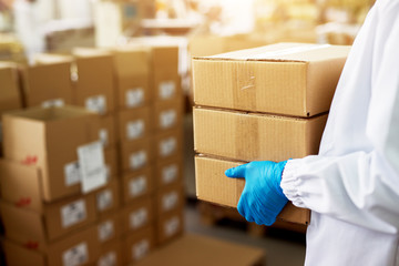 Close up view of a dedicated worker carrying a stack of duck taped brown boxes in factory storage...