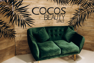 Soft green couch stands before a wooden wall with lettering 'Cocos Beauty Space'