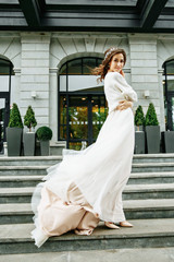 Beautiful bride in a white dress with long train is climbs up the stairs in a classic interior.
