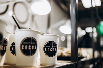 Paper cups with lettering 'Beauty Space Cocos' stand on the table