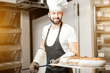 Baker carrying shovel with fresh baked breads standing near the professional oven in the bakery