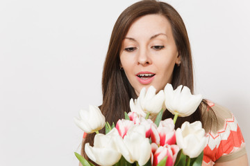 Close up portrait of beautiful young brunette girl is holding bright bouquet of white and pink tulips in hands, rejoices, looks at flowers in studio on white background. Celebration good mood concept.