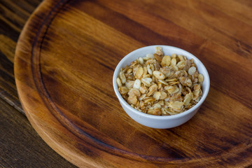 Granola or muesli in white ceramic bowl over wooden table.
