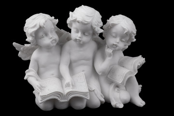 Three ceramic white angels read the book, dreaming and thinking. Isolated on black.