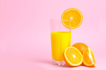 A glass with orange juice with the cut oranges on a pink background. Juicy color scale, pin up, pop up styles. Food for breakfast, a healthy drink with vitamins and miniroalami. A sunny drink.