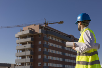 Architect or Engineer holding blueprints on the Construction Site. Daytime. Wearing protection equipment