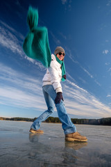 Girl in white jacke and flying blue scarf having fun while walking on ice on the frozen lake in winter