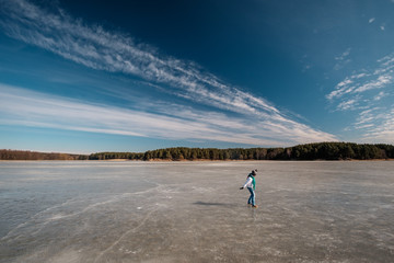 Girl in white jacket and blue scarf walking on ice on the frozen lake in winter
