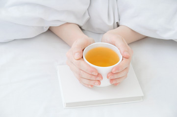 Fototapeta na wymiar Female hands from under the blankets hold a white cup of green tea in their hands