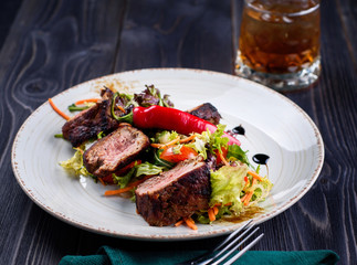 Veal salad with lettuce, carrot, tomato and pepper on white plate on dark wooden background, copy space. Restaurant food, close up. Meat salad and glass of whiskey