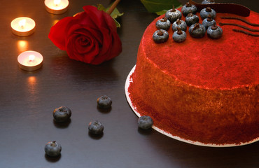 Cake red velvet on the table next to the rose adorned with blueberry berries and chocolate. Romantic evening by candlelight.