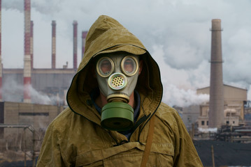 a man in a gas mask on a background of smoky pipes of a factory