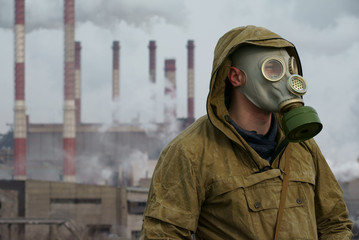 a man in a gas mask on a background of smoky pipes of a factory