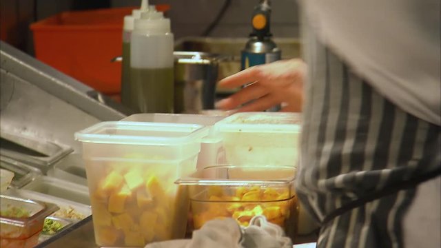 Close up shot of a chef moving Tupperware containers in a busy kitchen as him and another chef start to prepare something.