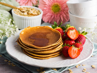 Stack of oatmeal flour pancakes with strawberries on white dish