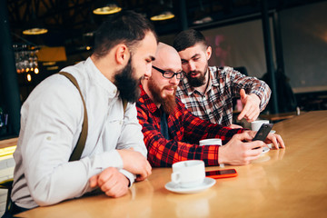 Friends of a man rest in a cafe , looking in the phone and discussing what they see