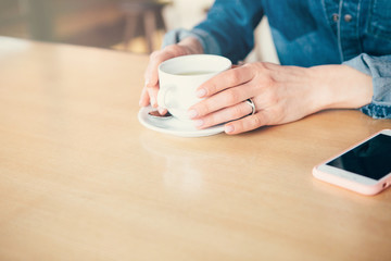 Close up shot of a woman halding a cup of fresh coffee sitting at the cafe with her laptop.