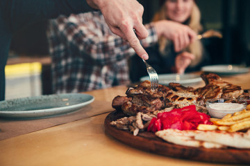 Attractive and happy friens having good time in cafe. They are smiling and eating meat.