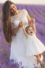 Fototapeta na wymiar Happy beautiful mother and cute little daughter have fun in aroma lavender fields. Family holiday in summer day.